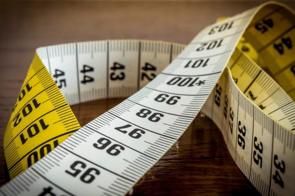 A measuring tape beside a bare foot and a shoe insole on a wooden floor